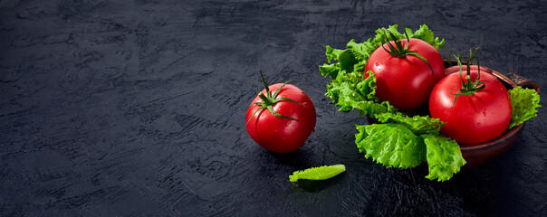 Fresh grape tomatoes with salad Leaves on black stone background. Vegan veggies diet food. Herb, red tomatoes, cooking concept.