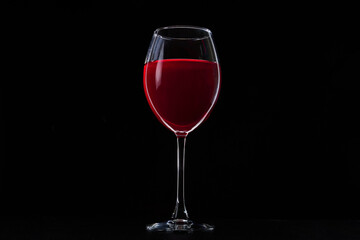 A glass of red vine on black background. Wine glass on dark table.