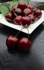 fresh sweet cherries on a white plate close-up on black wooden background