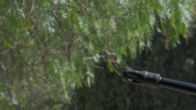 Close-up side view of the barrel of a G3 Assault rifle as it's being fired outdoors in a wooded area.