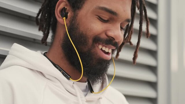 Pleased cheery african man outdoors listening music with earphones