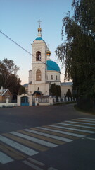 A modest white stone Church with blue domes and a straight bell tower on the opposite side of the road