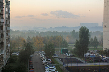 View from the window of a multi storey building on the Parking lot and the yellow forest in the fog behind it