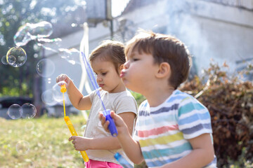 Little caucasian kids boy and girl blowing bubbles in a backyard.Shot of adorable sister and brother blowing bubbles outside.Blowing soap bubble with the best friend.Two kids having fun in the park.