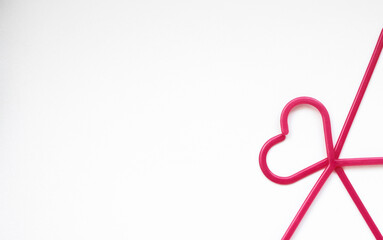 Pink coat hangers are stacked on top of each other in a heart shape in the right corner on a white background
