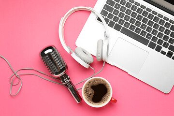 Headphones with microphone, laptop and cup of coffee on color background