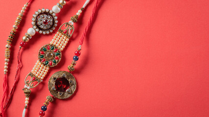 Raksha Bandhan, Indian festival with beautiful Rakhi on red background.  A traditional Indian wrist band which is a symbol of love between Sisters and Brothers.