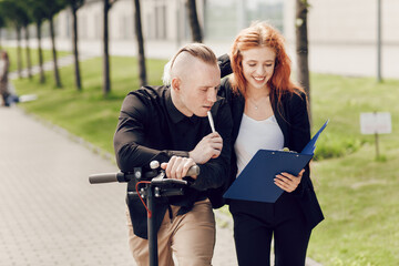 Fototapeta premium Close up portrait, man on scooter and redhead business woman outdoors at business meeting. Young people looking at a folder with documents. The latest technology, business concept