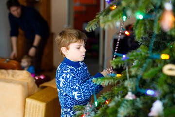 Little kid boy and his dad taking down holiday decorations from Christmas tree. Father on background. Family after celebration remove and dispose tree. Boys in festive clothes with reindeer