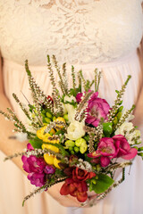 Bride holding bouquet of beautiful flowers in front of her wedding dress