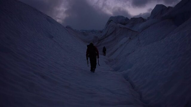 Clip of two men walking on a snowy mountaintop in  torres del paine national park, patagonia, chile, on a dark morning