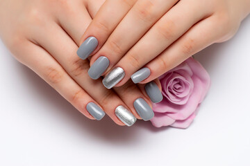 gray manicure with silver sequins on ring fingers on square long nails close-up on a white background with a pink rose in hands