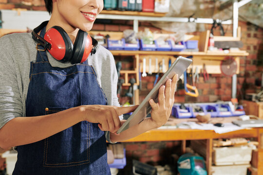 Cropped image of smiling female carpenter checking picture on tablet computer in search of inspiration for making new furniture item
