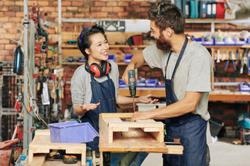 Smiling female carpenter talking to her coworker drilling screws when making wooden drawer