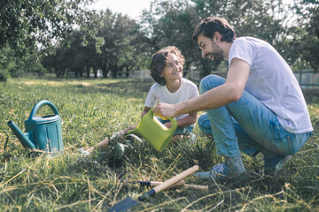 Dark-haired boy and his dad watering the plants in the garden