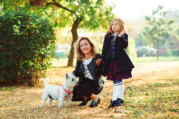 Fototapeta premium Happy family playing with dog in autumn park. Mother and daughter having fun together on a walk.