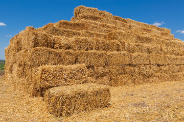 bales of yellow straw laid out in a stack similar to a pyramid, farmland during harvest