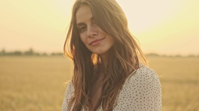Mystery pretty woman wearing dress touching her hair and looking at the camera while posing sideways on wheat field