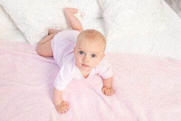 small baby girl 6 months old crawling on a white and pink bed at home, looking away, top view, place for text