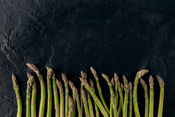 Raw uncooked green asparagus spears on black slate background. Concept of healthy nutrition, food and seasonal vegetables harvest. Close up