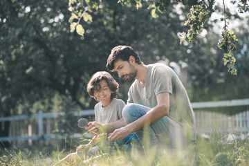 Dark-haired boy and his father looking at the plant through magnifying glass and looking involved