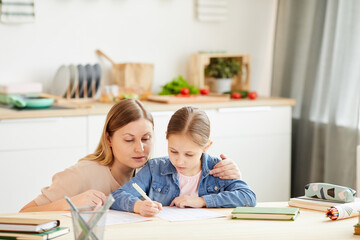 Warm-toned portrait of caring mother helping little girl do homework or study at table in cozy home interior, copy space
