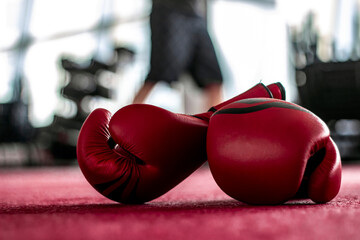 Pair of red leather boxing gloves on floor. Muscular built man getting ready for boxing exercise at...