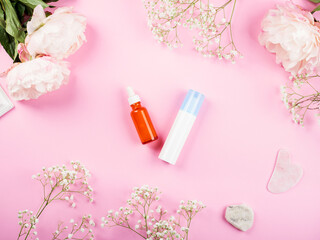 Pink background with skin care products generic bottles and floral decor. Flat lay