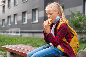 back to school. Girl wearing mask and backpacks protect and safety from coronavirus. Child eat sweet pastries for lunch near school. students new year.