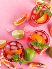 Naklejka premium Fresh iced red cocktail in pink glasses with blood orange and lime on pink background garnished with mint leaves. Closeup