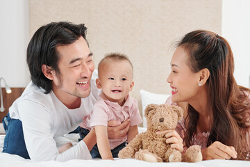 Happy young Vietnamese mother and father playing with little son in bedroom