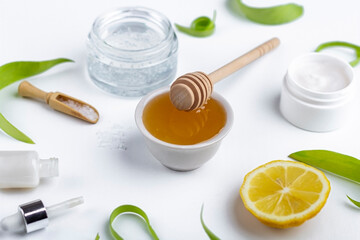 Natural organic ingredients to make home skin care. Cleansing and nourishing cosmetics. Beauty products: cream, honey, sea salt among green leaves on white background. Close up, copy space for text