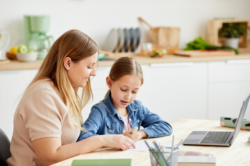 Warm-toned portrait of caring mother helping cute girl doing homework or studying at table in cozy home interior, copy space