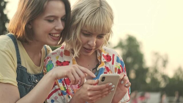 Two attractive young girls are discussing something while watching in the smartphone walking in the park