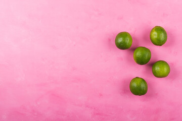 Fresh whole green limes on pink background. Summer color mockup flat lay backdrop
