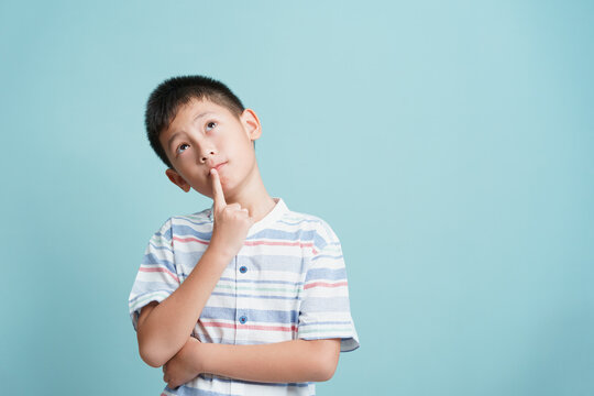 Asian little boy standing thinking on blue background isolated