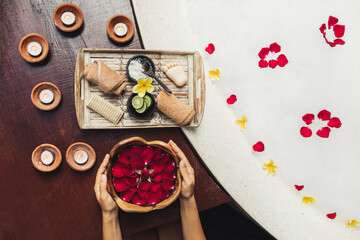 Obraz na płótnie Canvas Woman hands holding wooden bowl with red rose flower petals. Romantic spa set with lime, scrub, salt, towels and brush on wooden tray. Organic and natural beauty treatment.