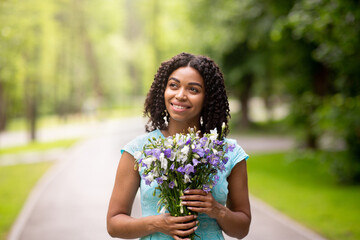 Portrait of pretty black lady holding bouquet of flowers in countryside