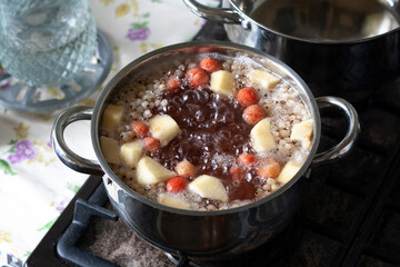 Fruit and berry compote boils in a pot on the stove in the kitchen