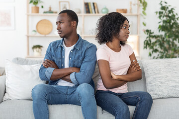 Offended black husband and wife sitting on couch at home