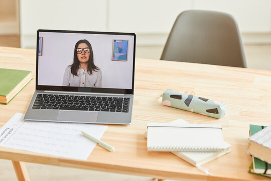 Background image of wooden desk with school supplies and laptop with female teacher giving video lesson or online class on screen standing on wooden desk with school supplies, copy space