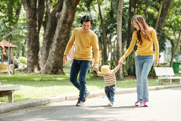Happy young father and mother holding hands of baby boy when walking together in park