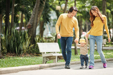 Obraz premium Happy young Vietnamese family with little son walking in park on sunny day