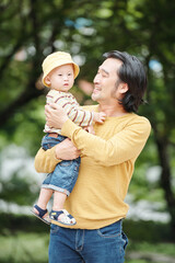Fototapeta premium Joyful young father enjoying being a parent, he is carrying little son and looking at his with love