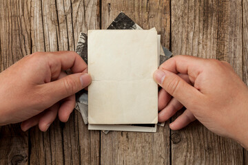 Old vintage photo template (mockup) in hands on wooden background. Empty retro card, textured paper.