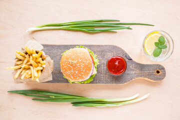 Top view burger, french fries, sauces and lemonade on wooden background