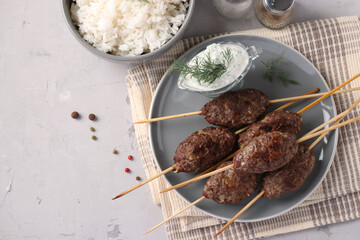 Kofta kebab on wooden skewers on a plate with sauce and a side dish of rice on the table, traditional dish of Arab cuisine, grilled minced meat shish kebab