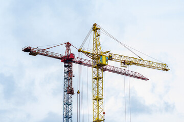 Two high cranes for house building at construction site on blue sky background.