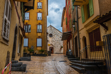 Fototapeta premium A picturesque wide angle view of a narrow street in a medieval French village in the Alps on a rainy day (Puget-Theniers, Alpes-Maritimes, Provence, France)