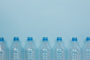 Empty clear plastic bottles without caps stacked on a blue background. Recycling and environment concept.